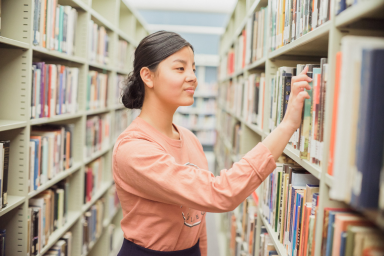 student looking through books on a bookshelf