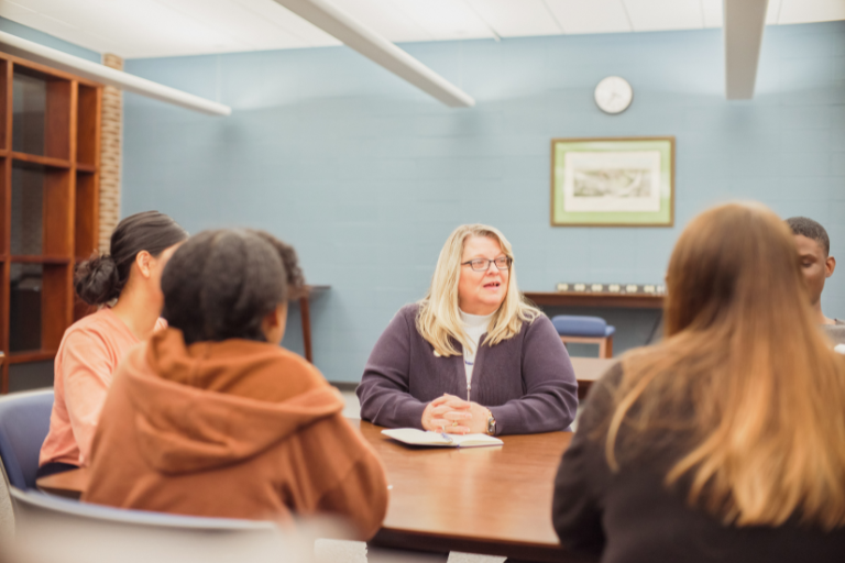 adult sitting and speaking with students at table